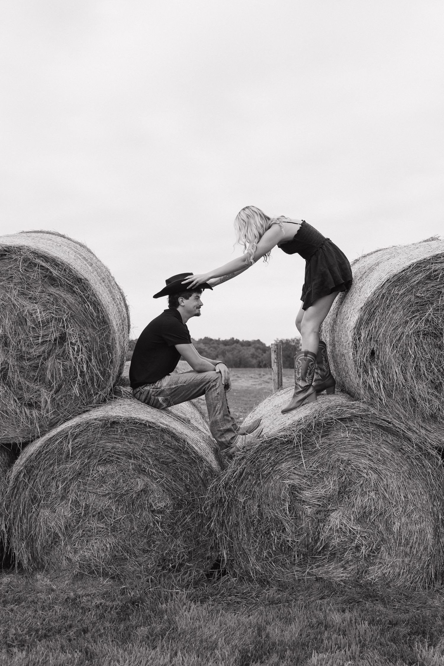 Two people, a man and a woman, are climbing on top of large hay bales in a field.
