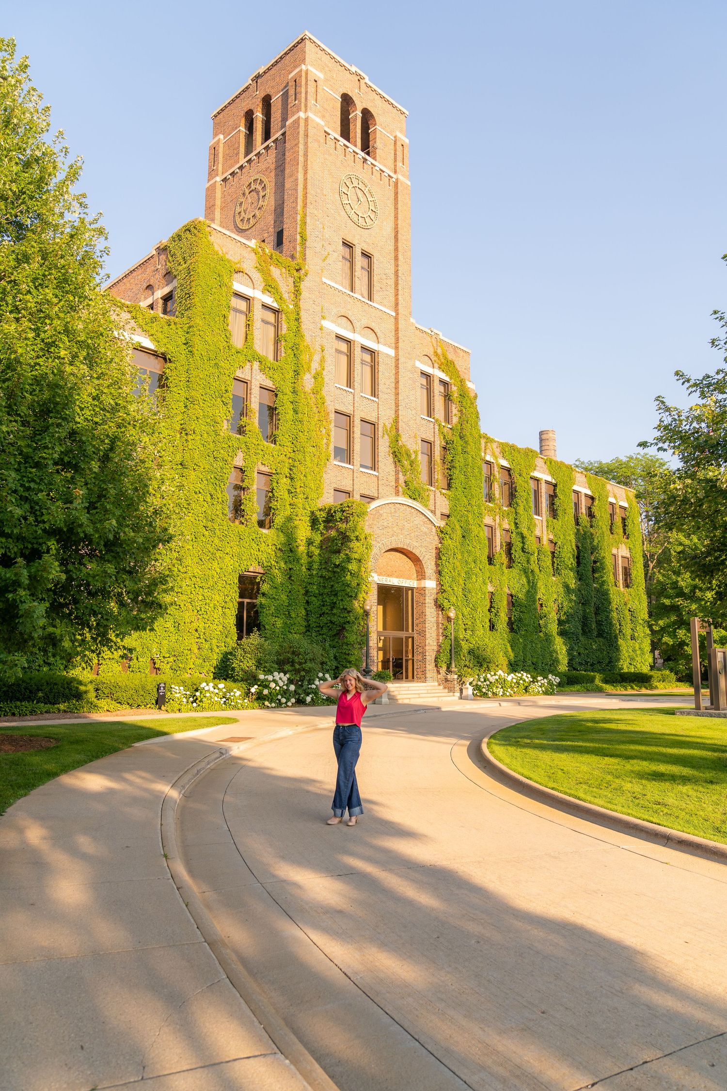 A historic brick building with ivy-covered walls and a tall tower, surrounded by a lush green lawn and winding pathways.