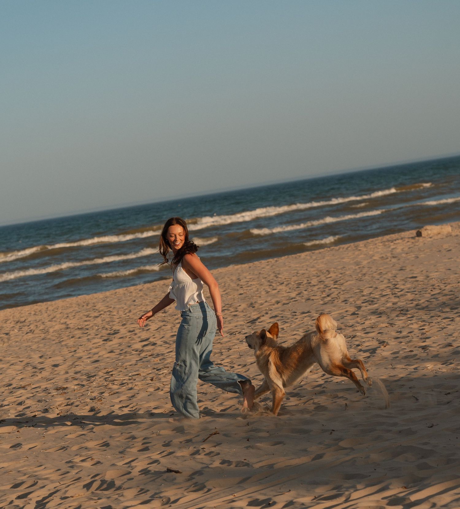 A woman walking on a sandy beach with two dogs running alongside her.