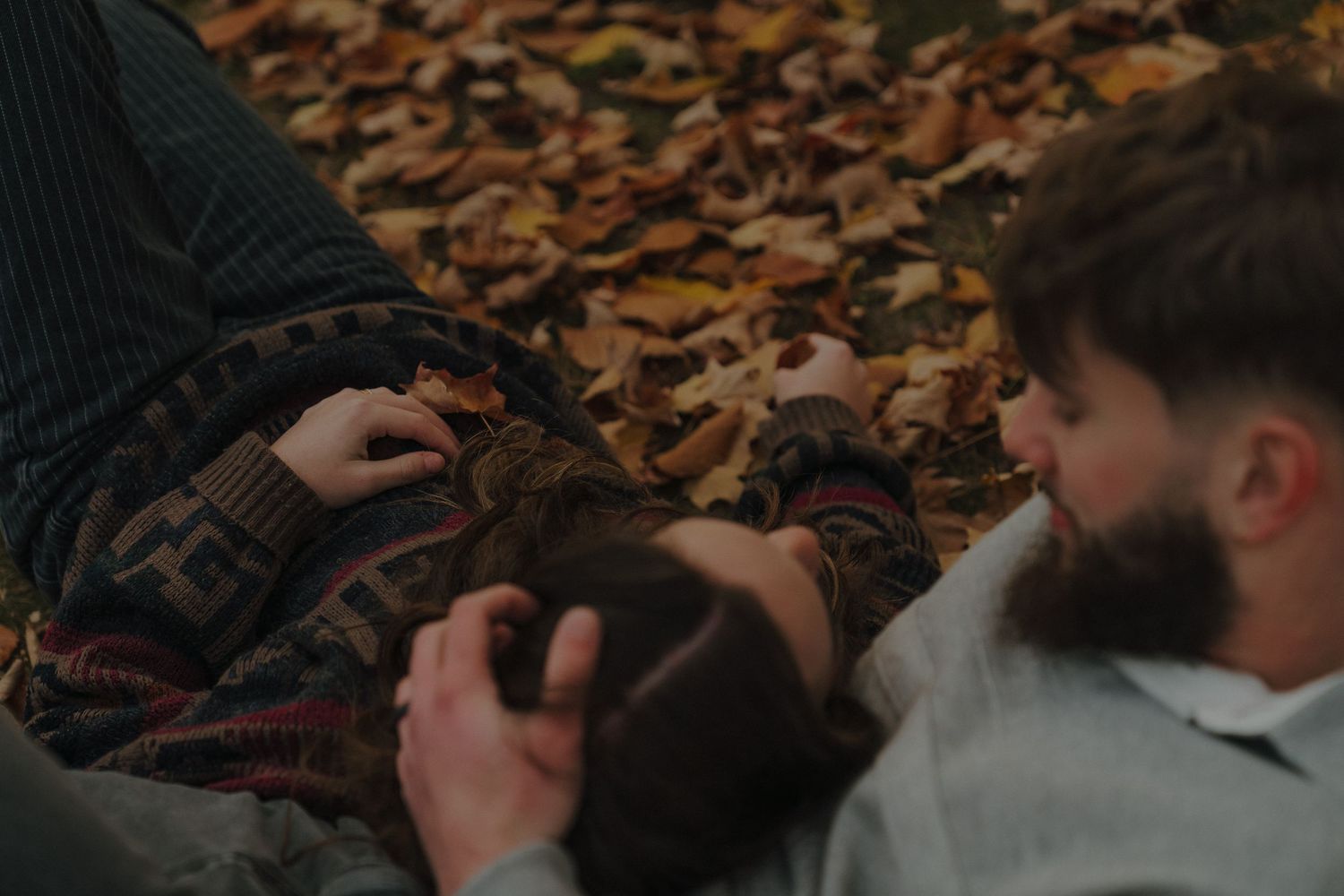 Two people are sitting together on the ground surrounded by fallen autumn leaves.