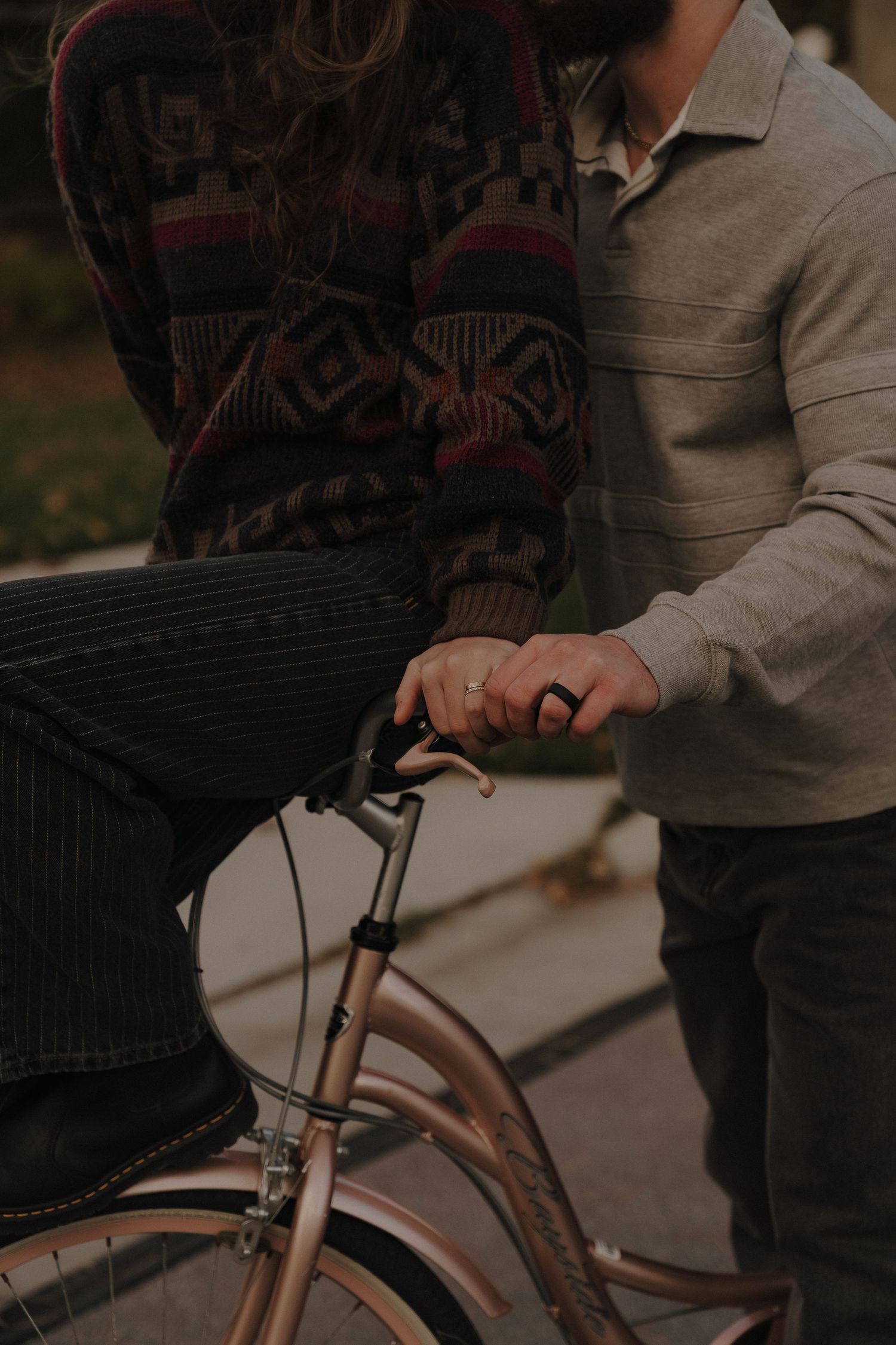 A person wearing a patterned sweater is locking a bicycle with a lock on a city street.