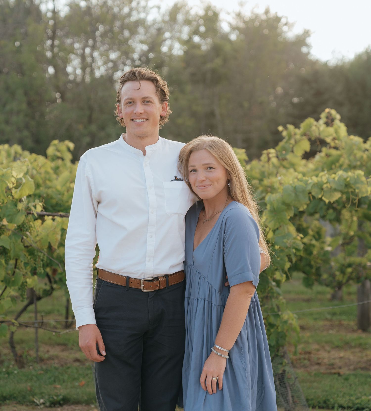 A happy couple standing together in a vineyard, smiling and embracing.