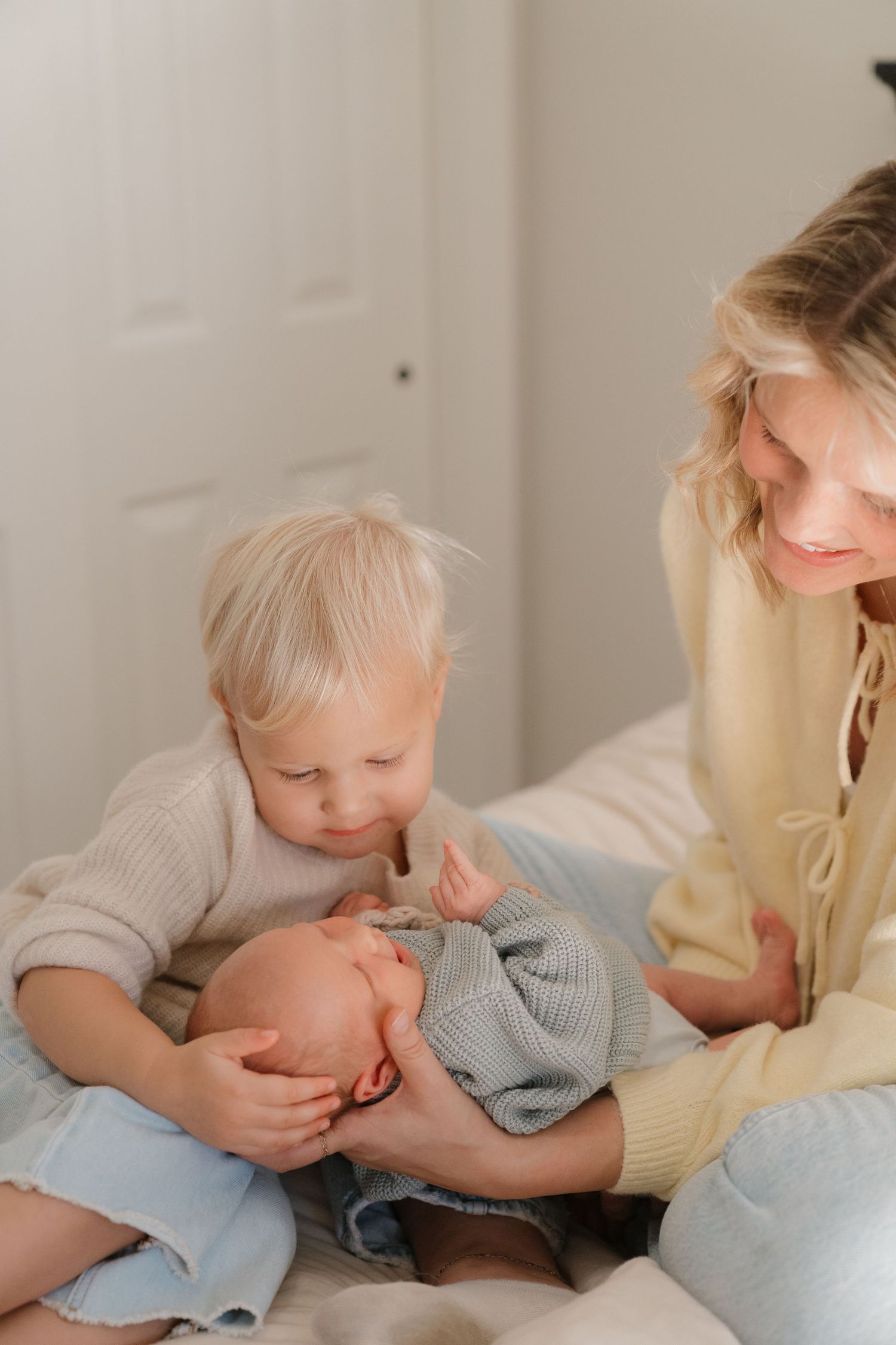 A mother sitting on the floor cuddling and holding her young child, who appears to be an infant.
