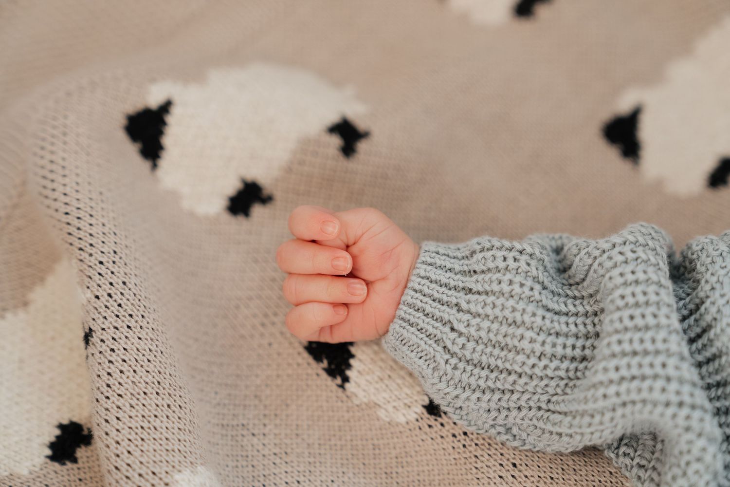 A close-up view of a baby's hand peeking out from a cozy, patterned blanket.