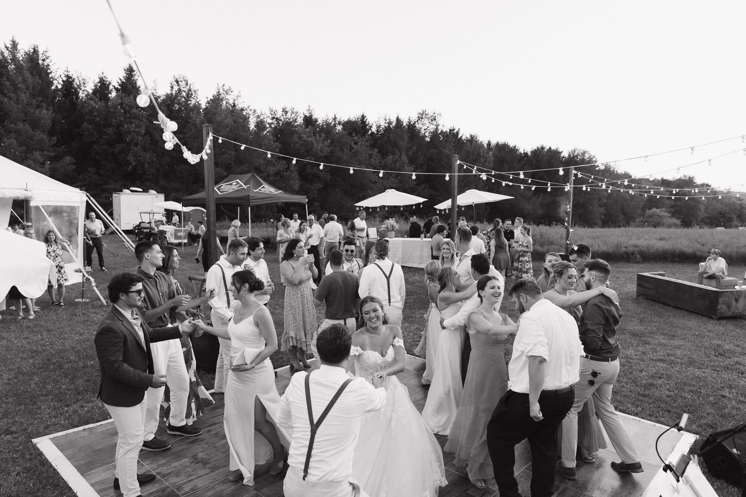 A black and white image of a crowd of people gathered at an outdoor event, with tents and decorations visible.