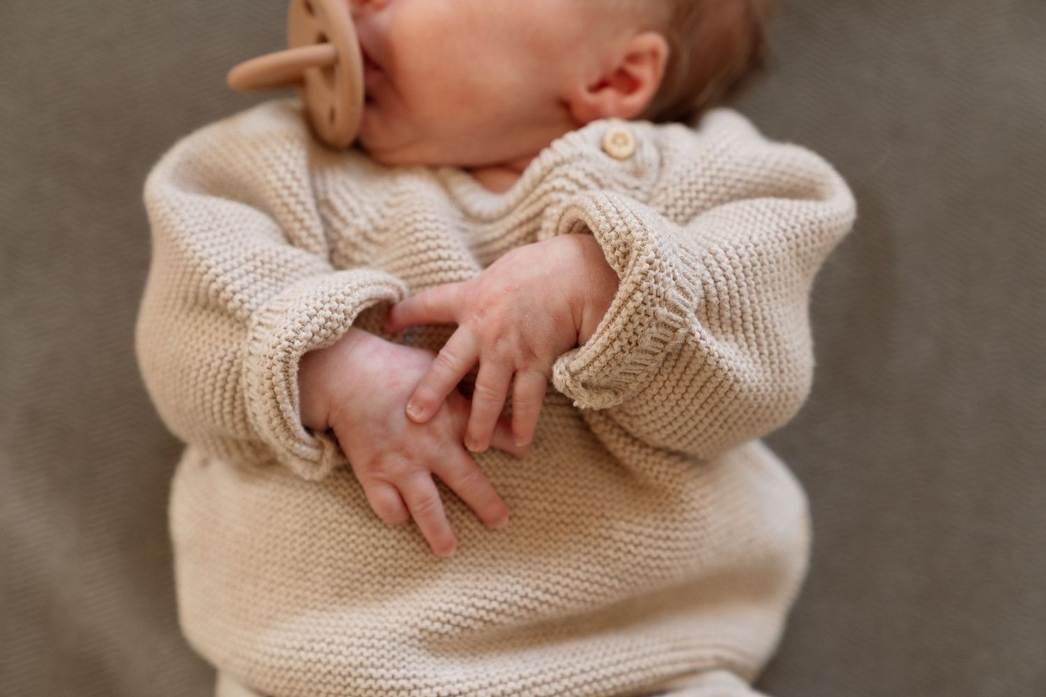A newborn baby swaddled in a cozy beige sweater, resting peacefully.