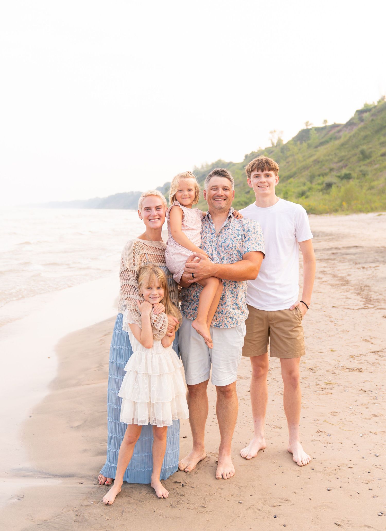 A family of five, including two adults and three children, standing together on a beach.