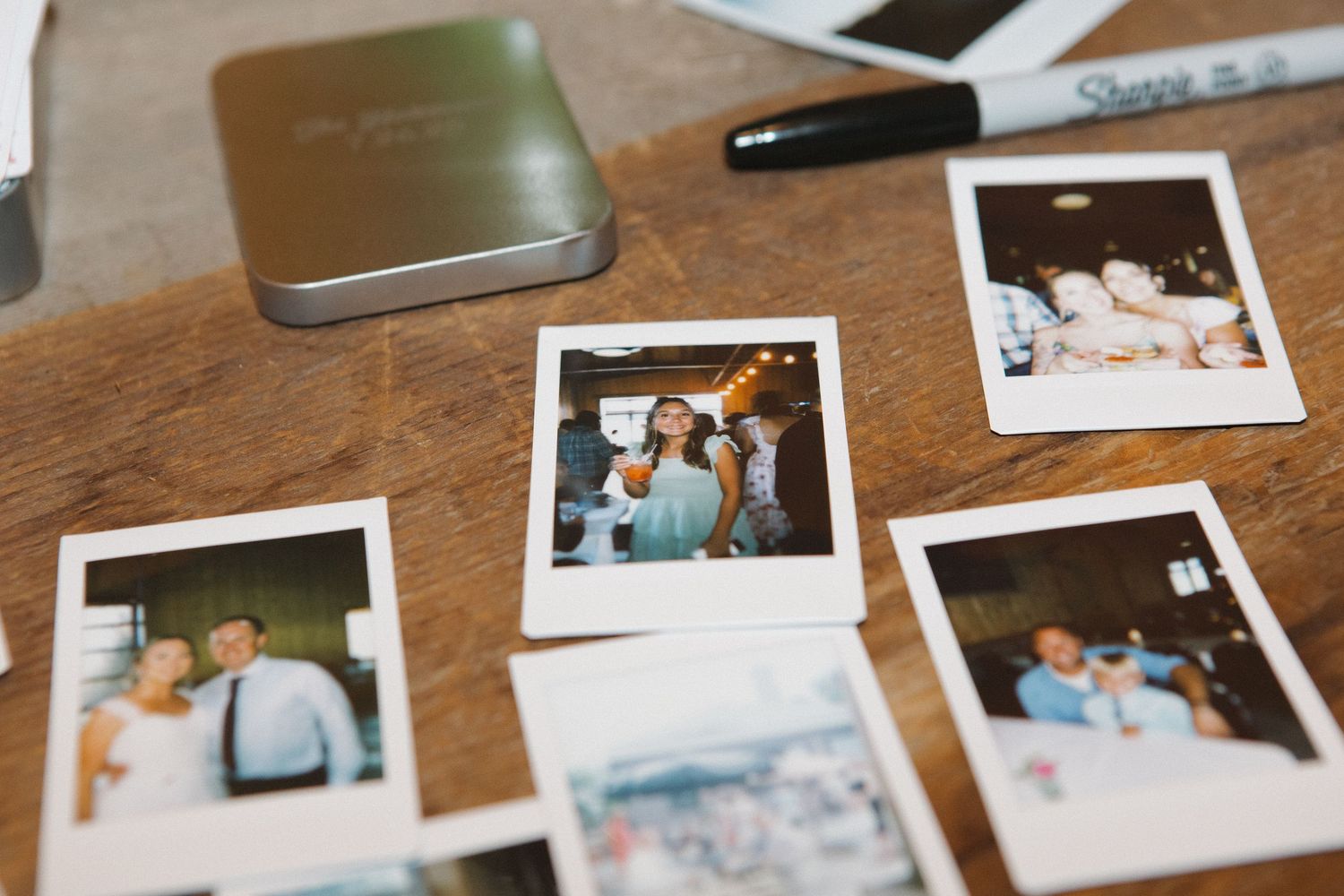 A collection of polaroid photos showing people in various settings on a wooden table.