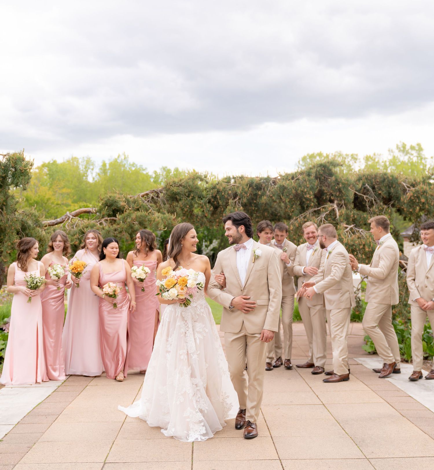 A wedding party poses on a wooden deck surrounded by trees and greenery.
