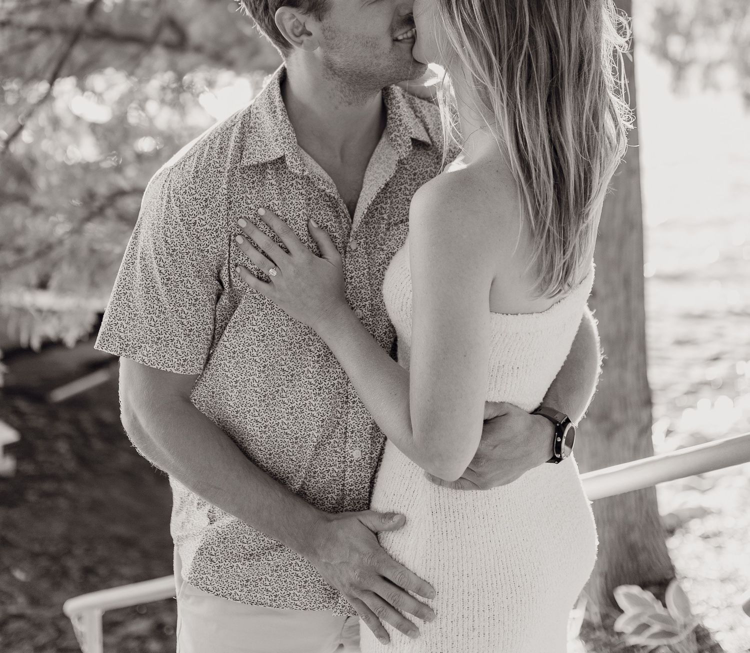 Black and white photo of a couple sharing a romantic kiss outdoors during an engagement session.