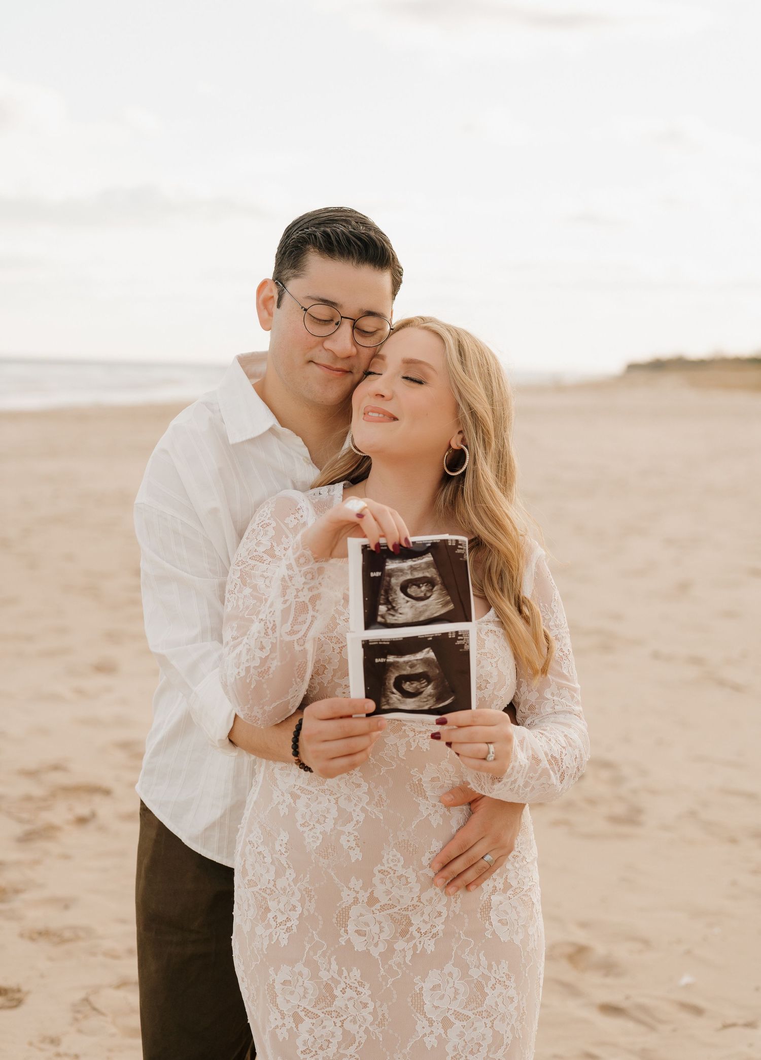 A couple embracing on a beach, with the woman holding an ultrasound image.