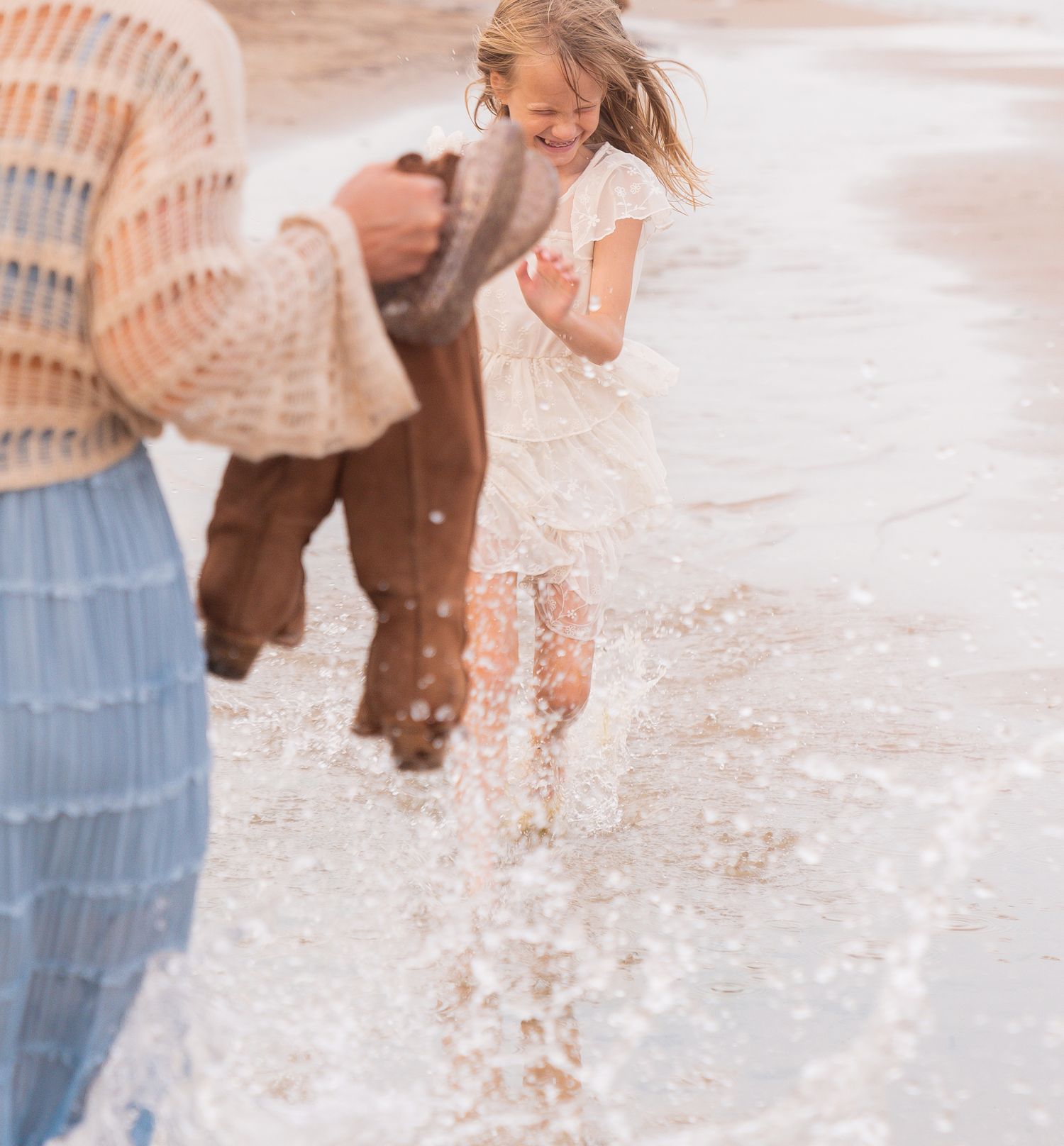 A woman in a white lace dress walks in the water playfully.