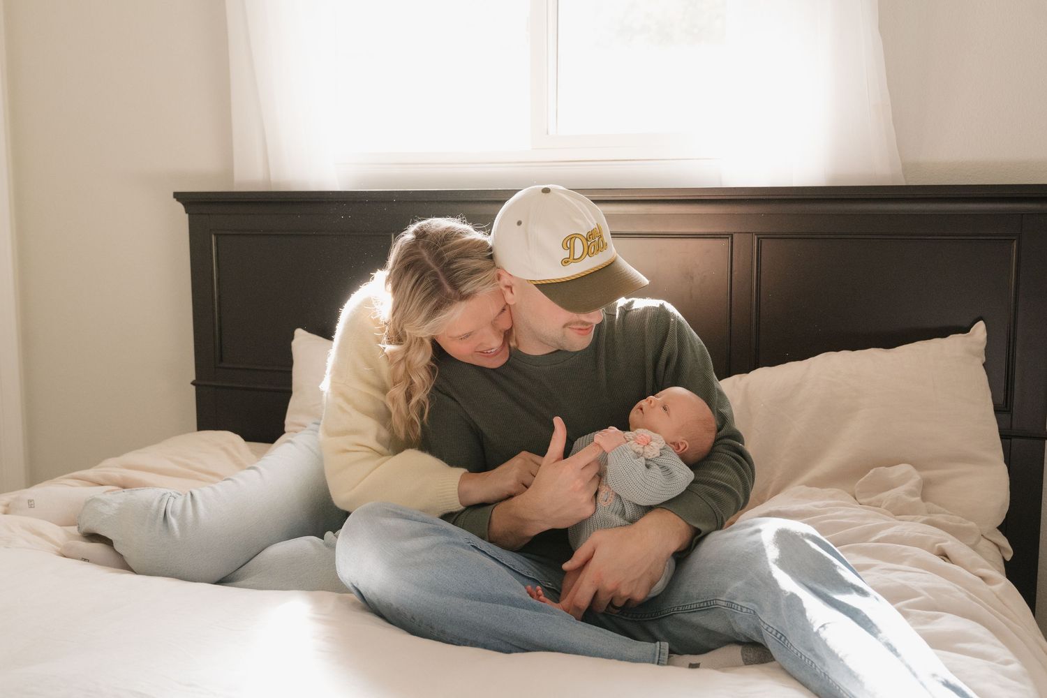 A couple embracing and holding a newborn baby on a bed.