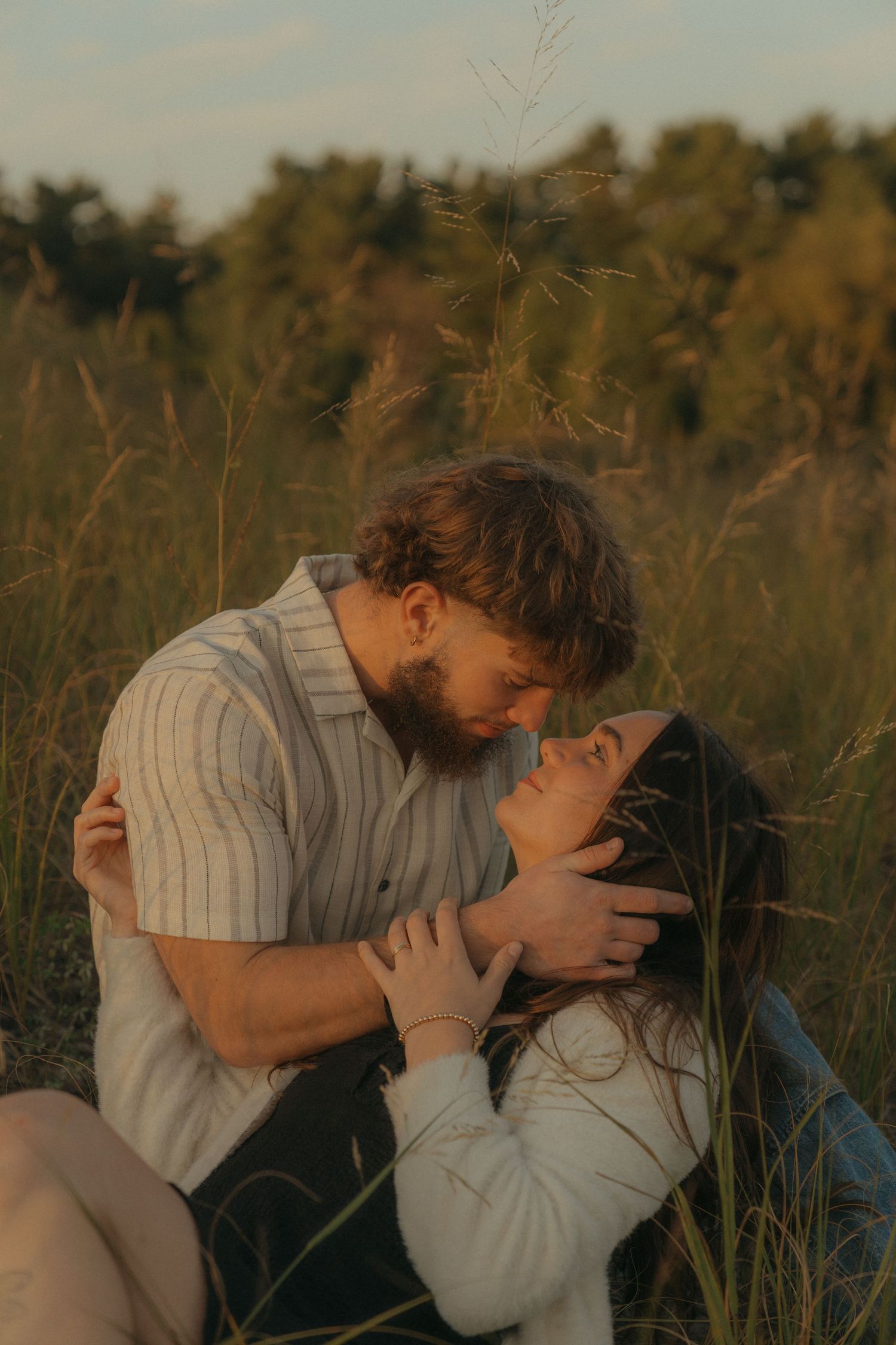 A couple embracing in a field of tall grass on a sunny day.