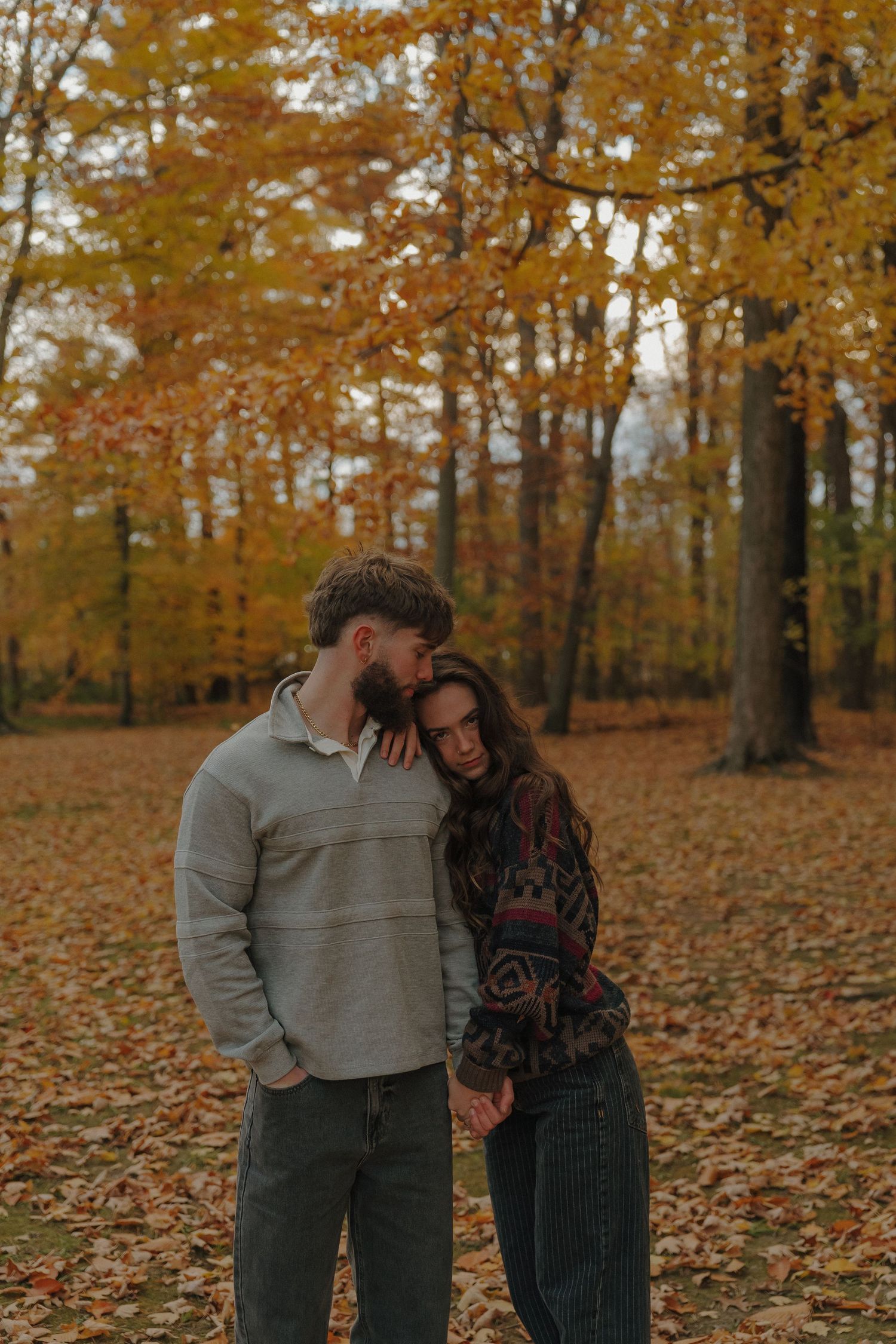 A couple embracing in a colorful autumn forest, with orange and yellow leaves surrounding them.