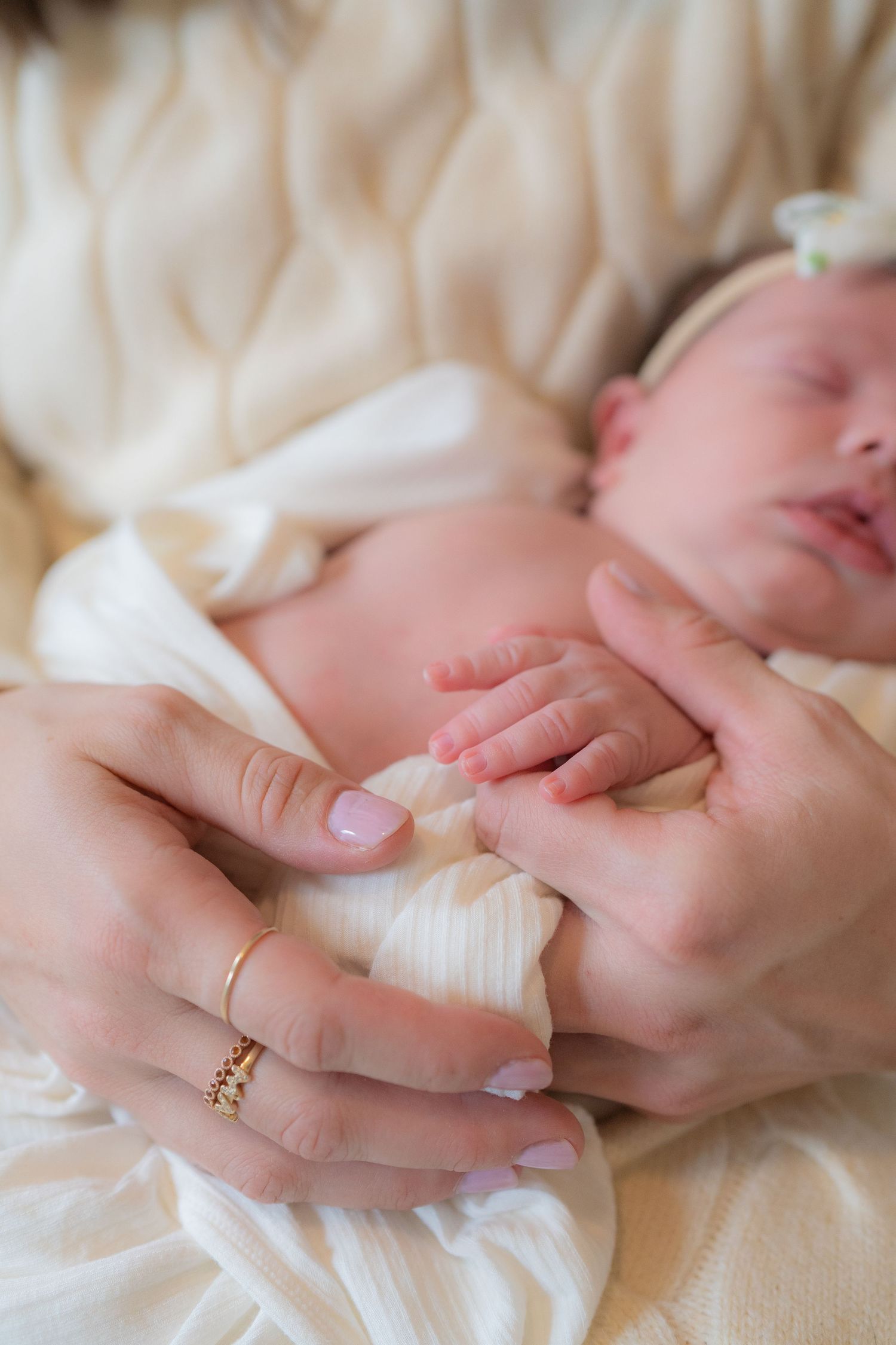 A newborn baby's tiny hands are gently held by an adult's hands, showing the tenderness and care of a parent or caregiver.