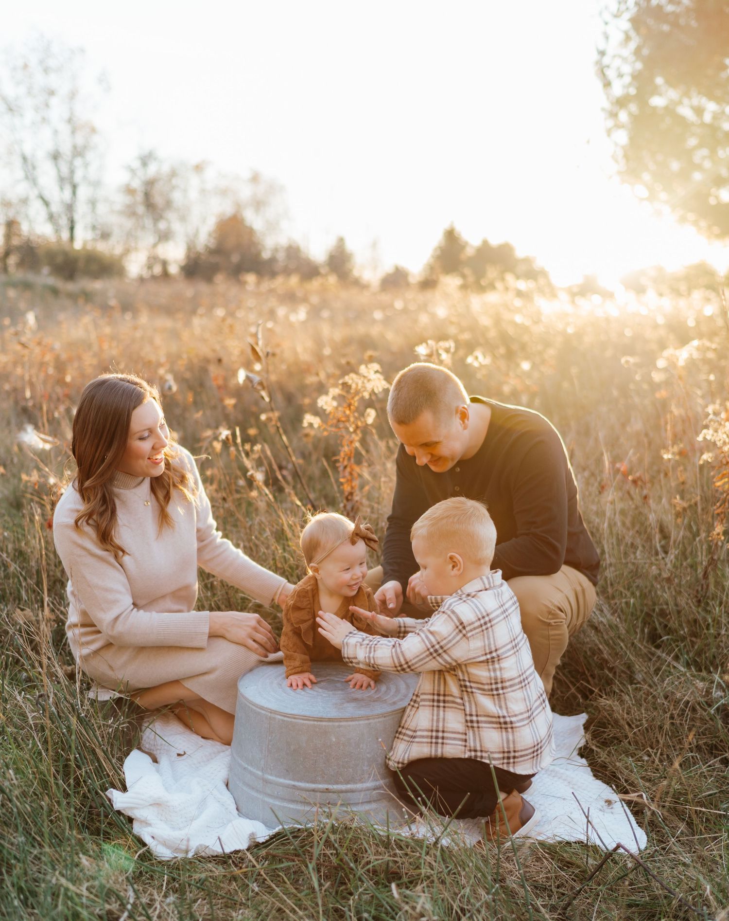 Family of four enjoying a golden hour outdoor photo session in an autumn field with warm sunlight.