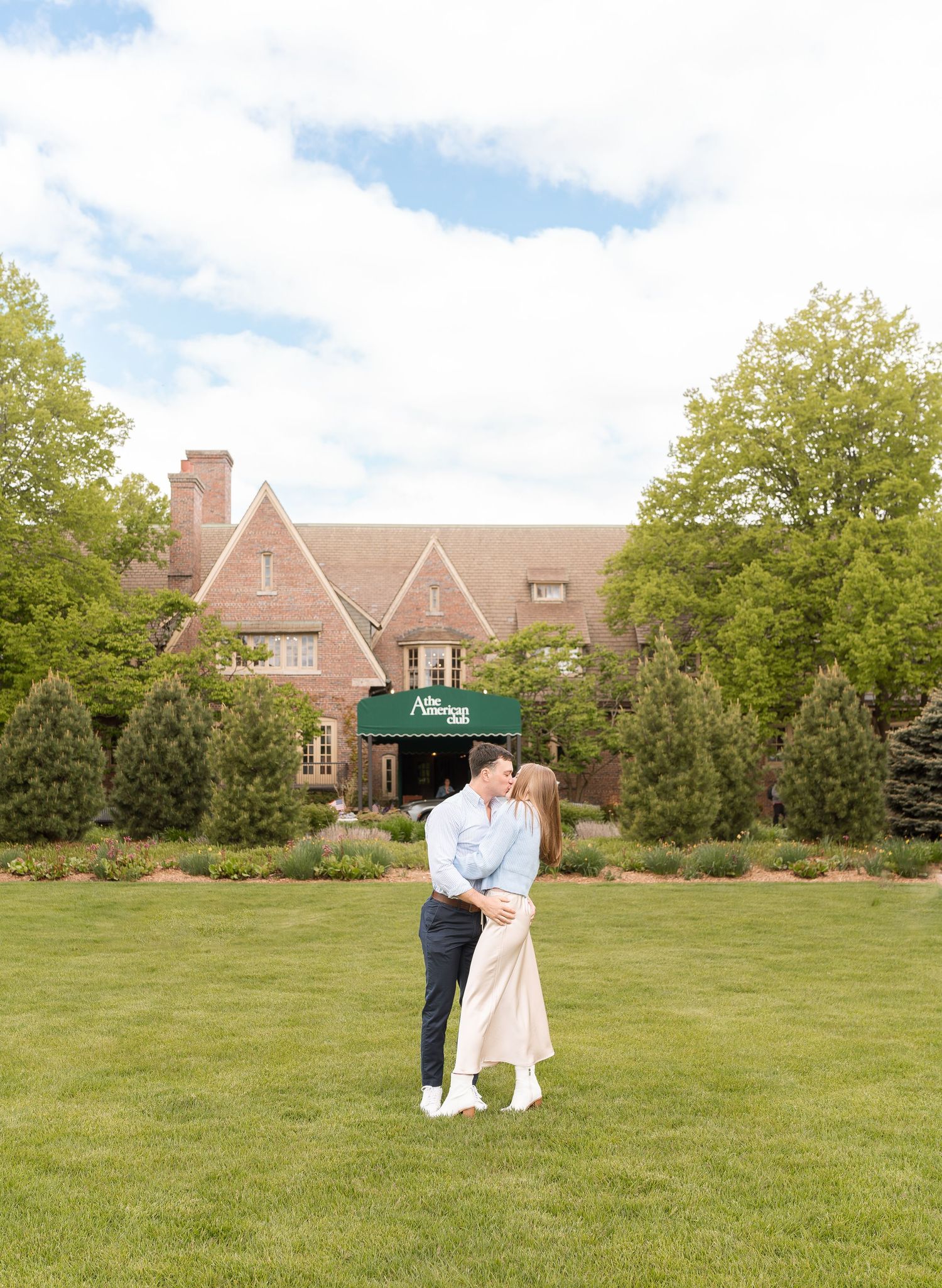 A couple embracing in a lush garden with a historic building in the background.