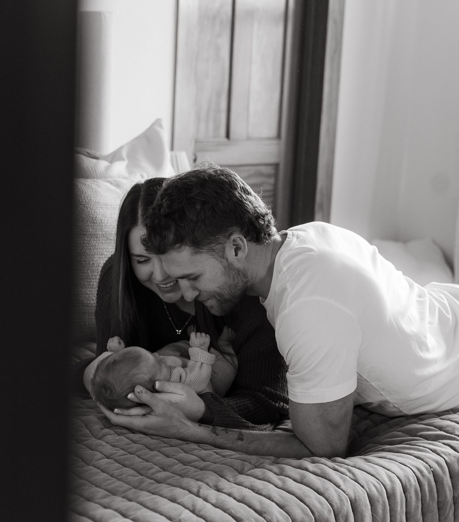 A man tenderly holds a newborn baby in his arms on a bed.