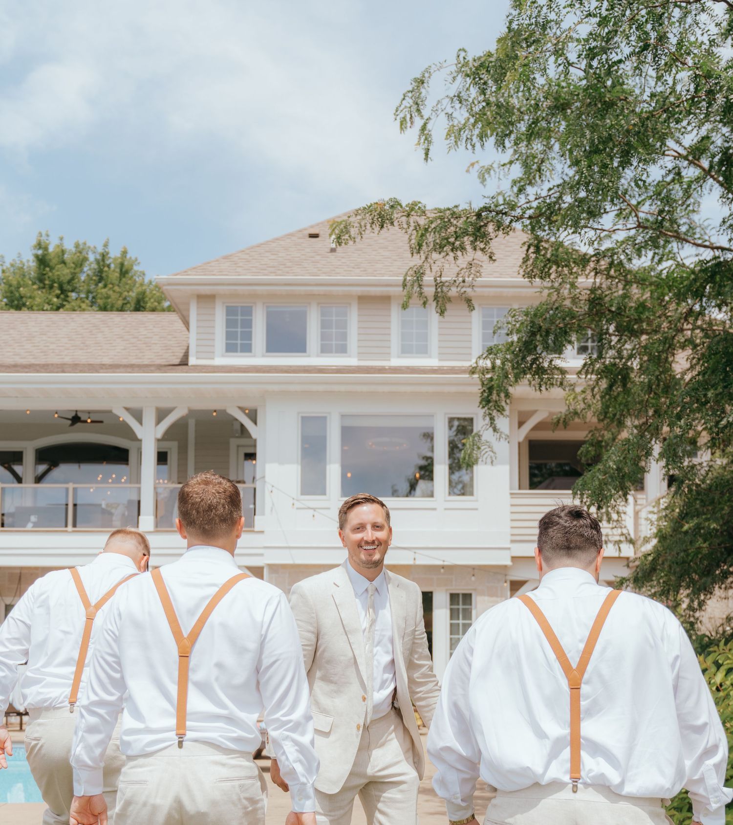 A group of men in white suits standing in front of a large white house with a porch.