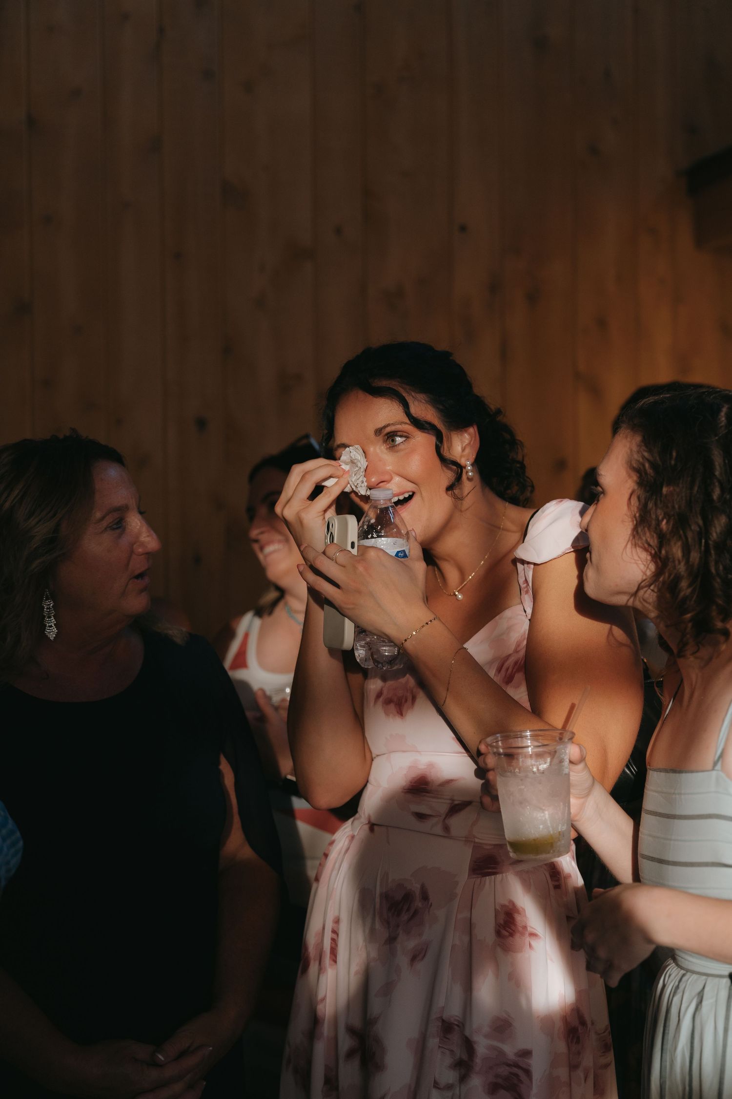 The image shows a group of women laughing and enjoying drinks together in a cozy, rustic setting.