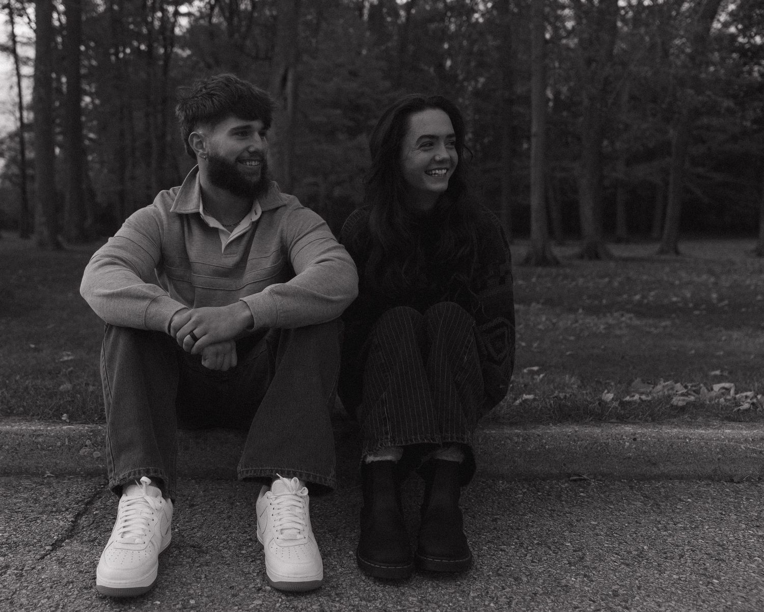 A black and white image shows a man and woman sitting on a bench in a forested area.