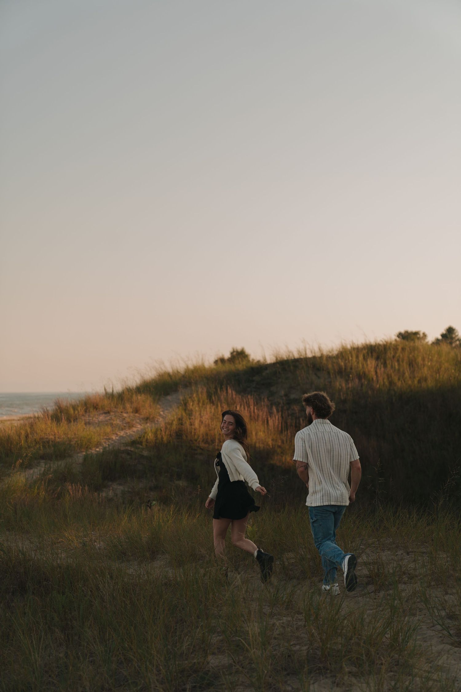Two people walking on a path through a grassy field at sunset.