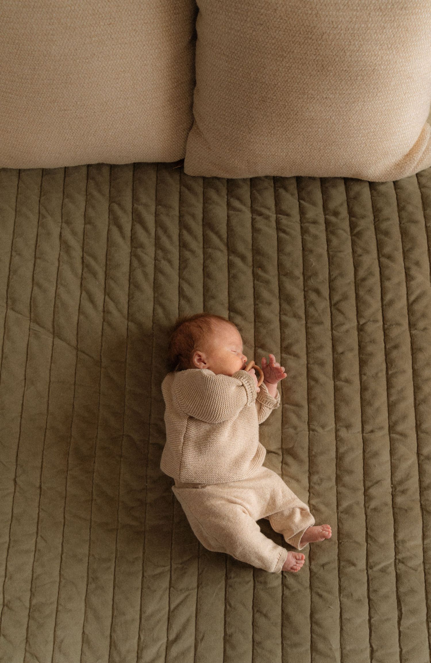 A sleeping newborn baby is curled up on a quilted blanket.