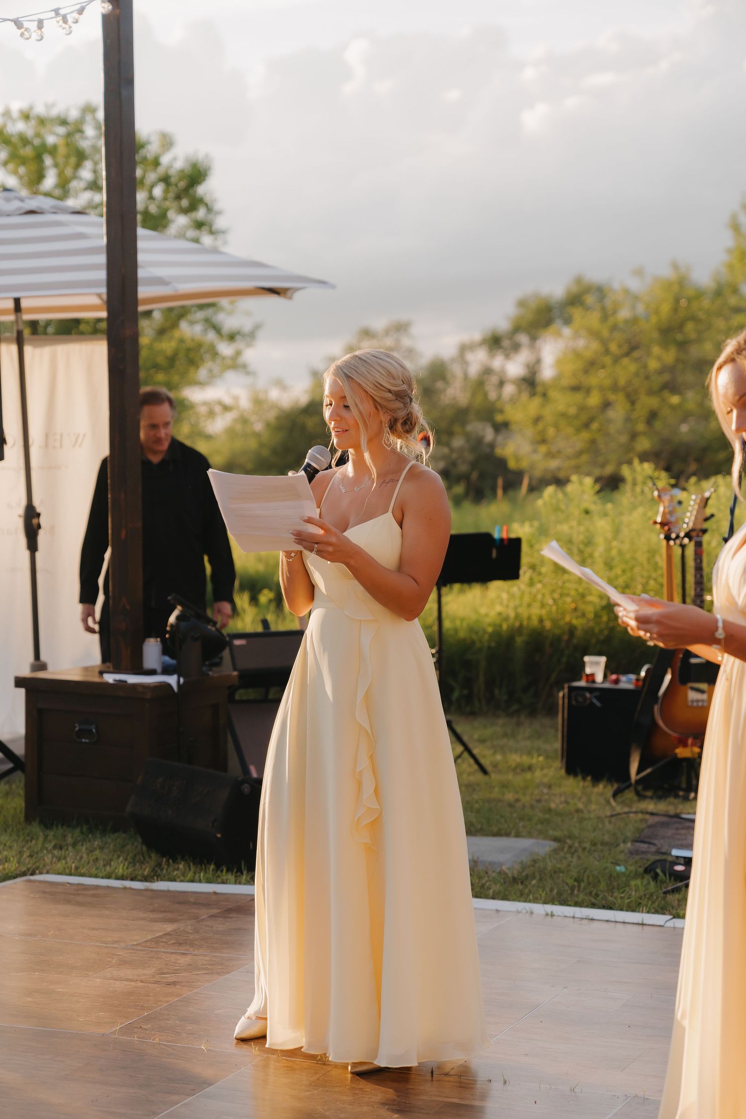 A woman in a white dress stands on a dance floor at an outdoor event.