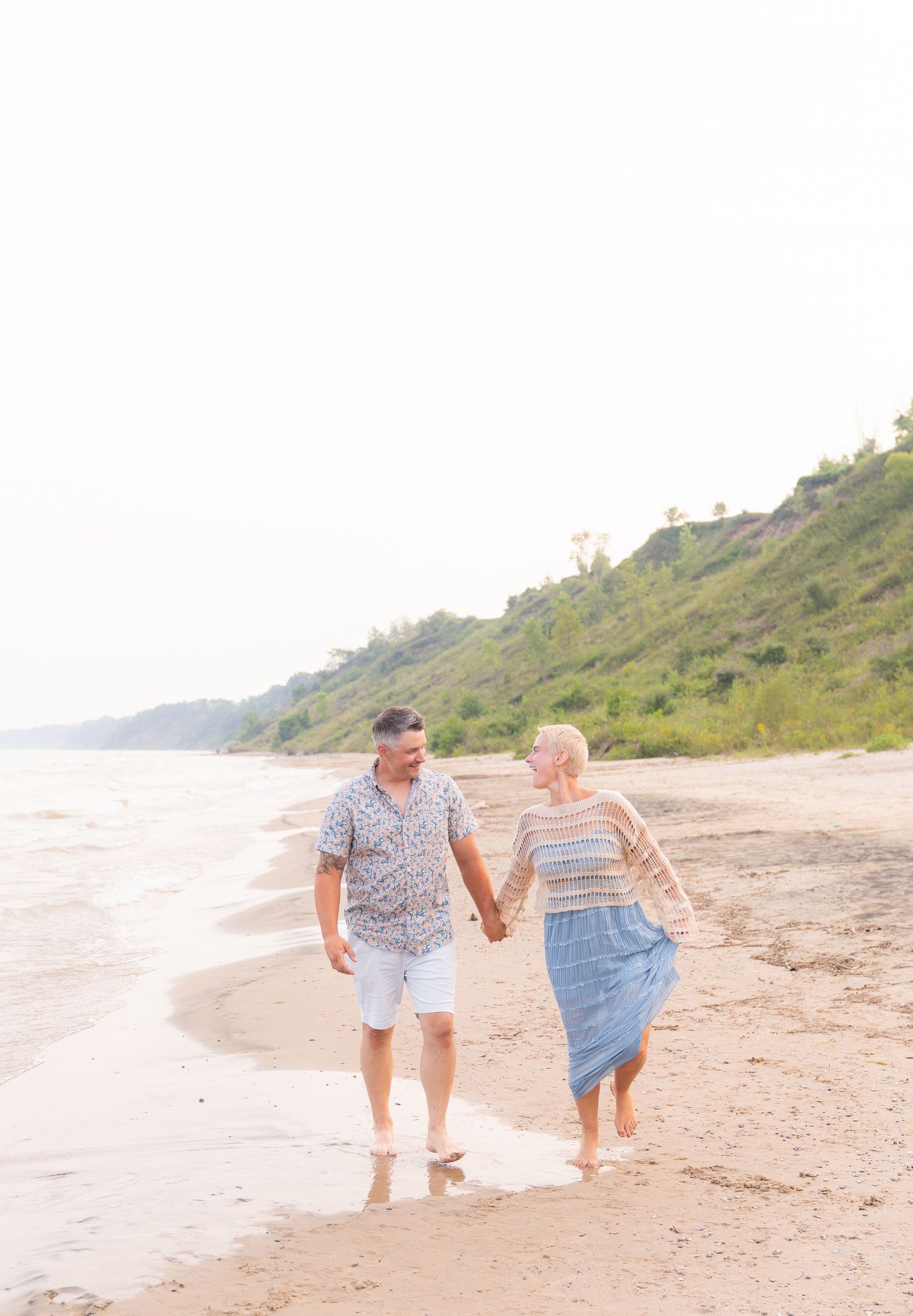 A couple walks hand-in-hand along a sandy beach, enjoying the scenic coastal landscape.