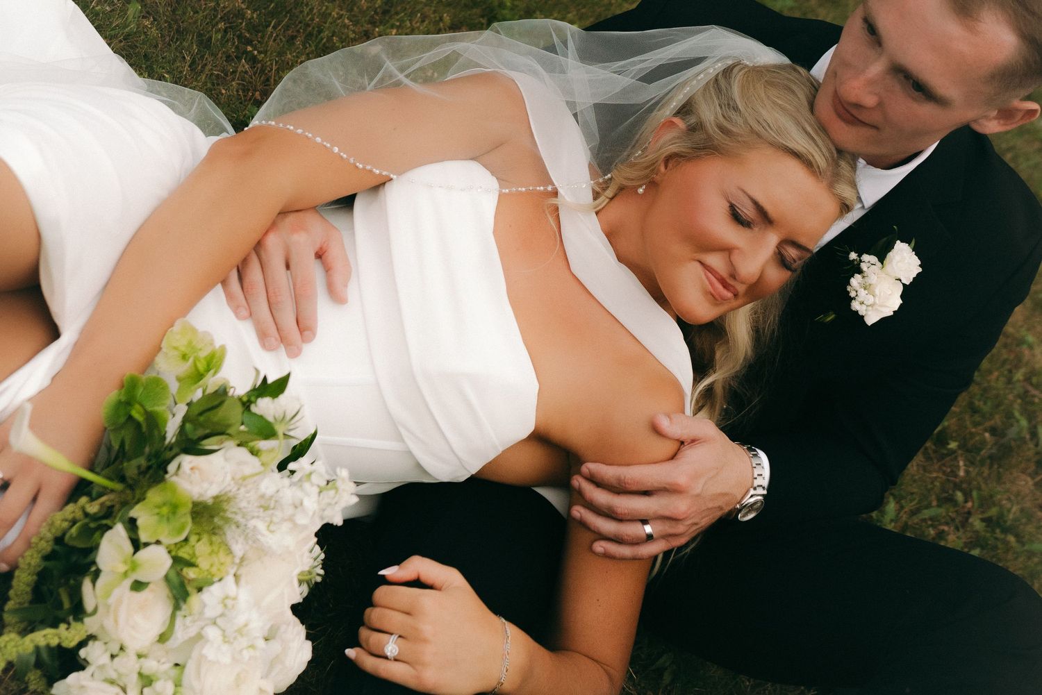 Bride and groom sharing a romantic moment outdoors, bride in white gown holding bouquet, groom in black tuxedo.