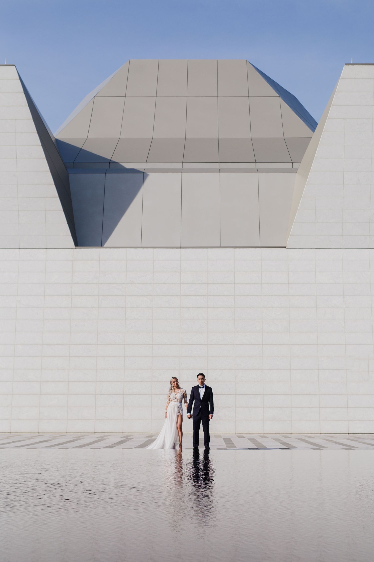 Minimalist architectural wedding photos showing couple against white geometric building with reflective pool.