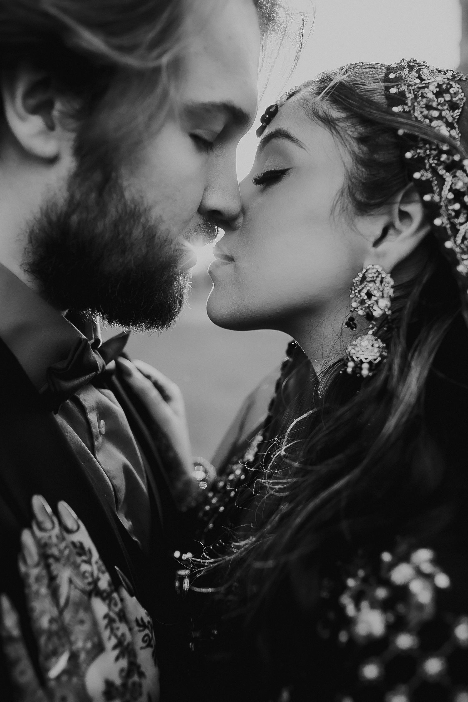 Romantic black and white portrait of couple sharing intimate kiss with ornate accessories.