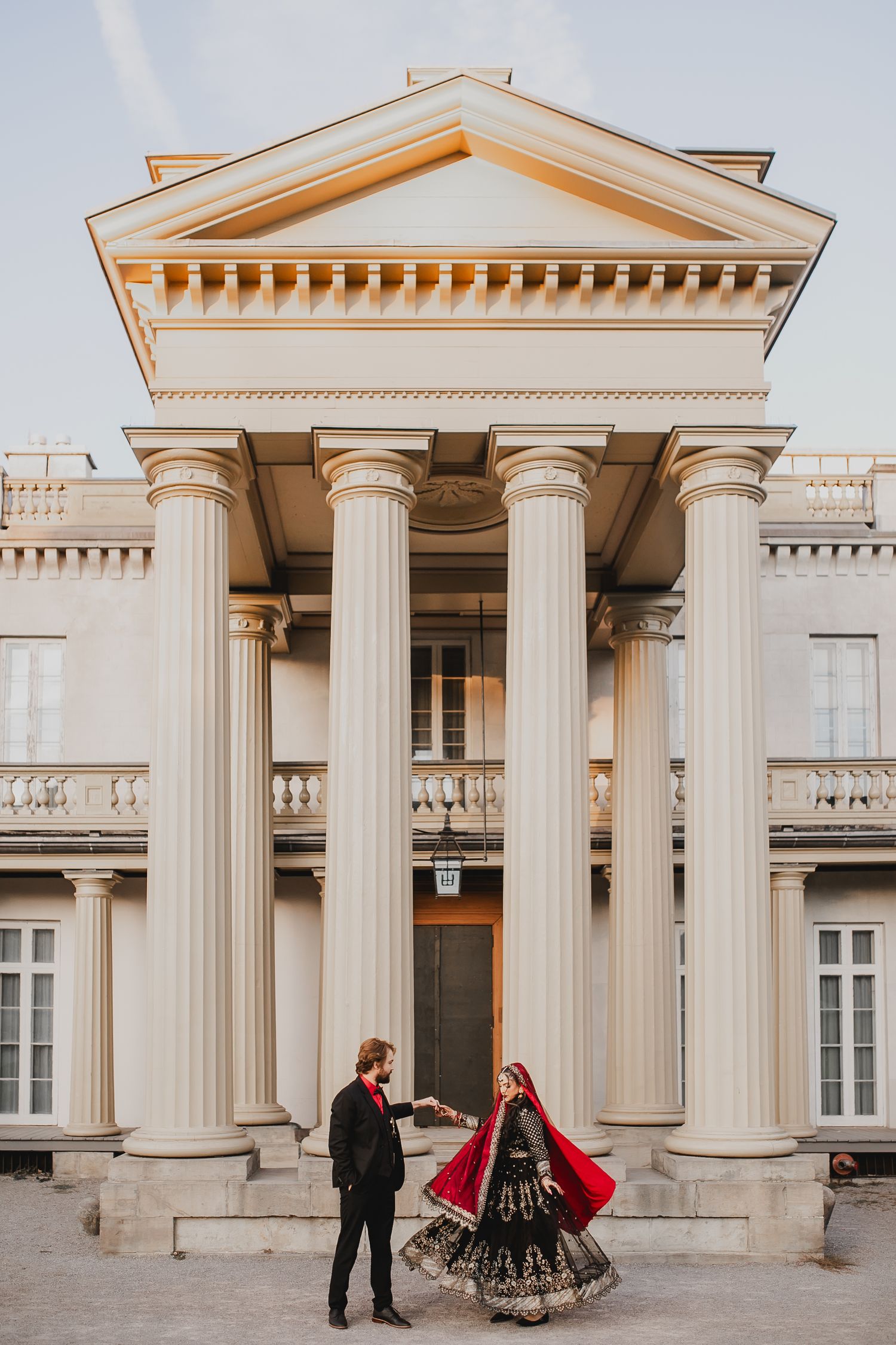 Wedding couple poses against classical white columned architecture.