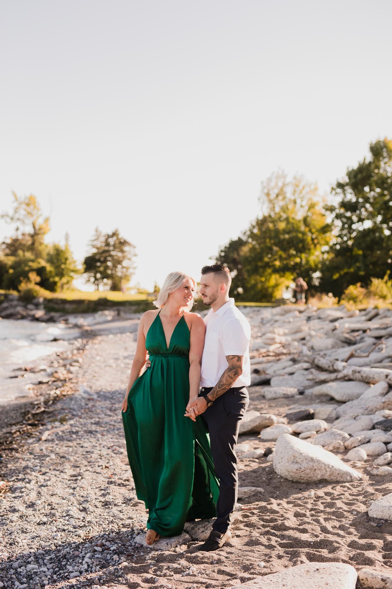 A couple sits together on a rocky beach at sunset in a romantic outdoor photoshoot.