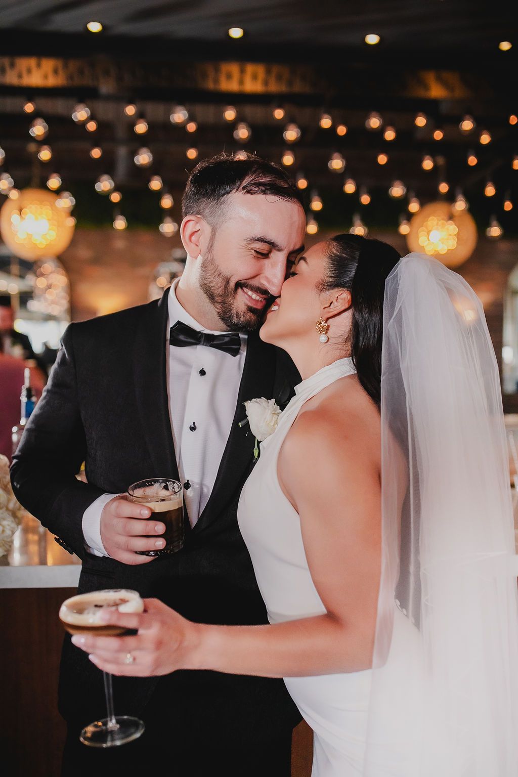 Romantic newlyweds share intimate moments while holding champagne glasses during their wedding reception celebration.