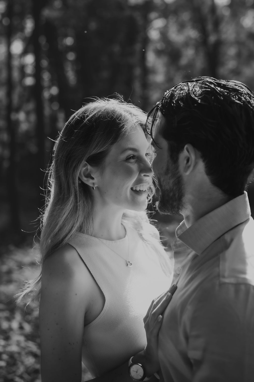 A romantic black and white portrait of a couple sharing an intimate moment in a sunlit forest setting.
