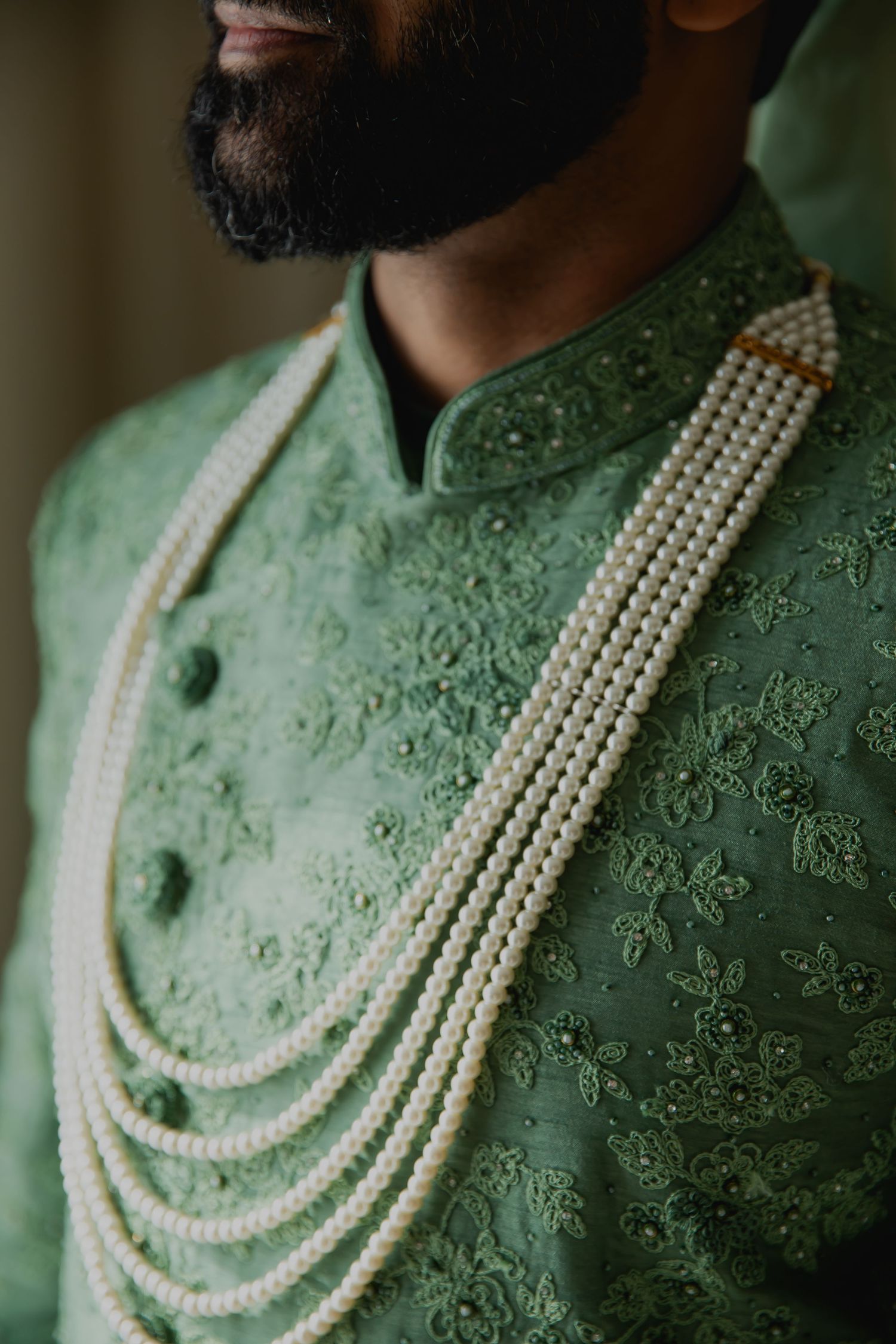 Close-up of mint green embroidered sherwani with pearl necklace detail.