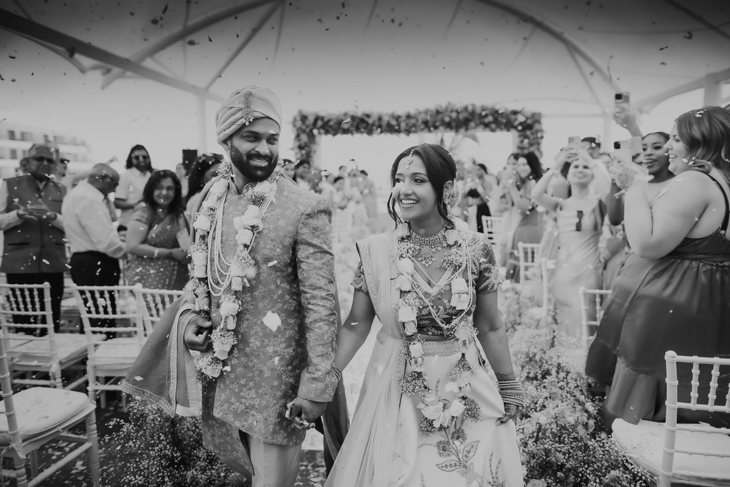 Couple walking down aisle after ceremony while guests celebrate with flower petals.