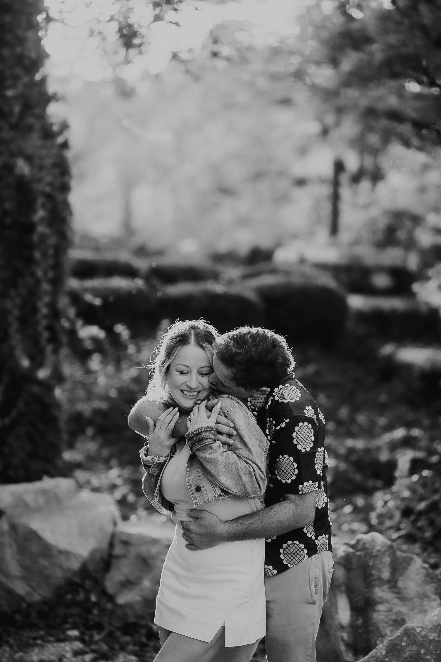 Candid black and white photo of couple embracing in garden setting.