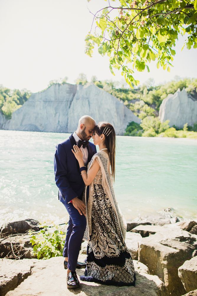 A romantic couple shares an intimate moment on rocky shores beside turquoise waters at Scarborough Bluffs.