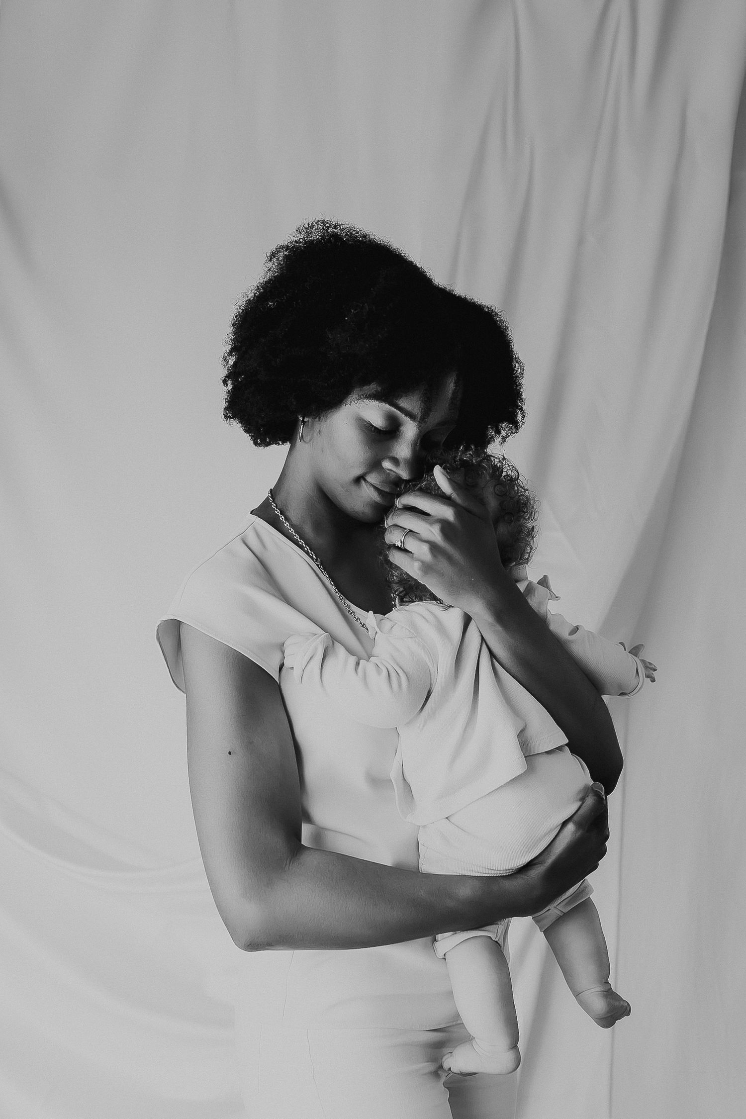 Black and white photo series showing tender embrace between mother and baby against white backdrop.