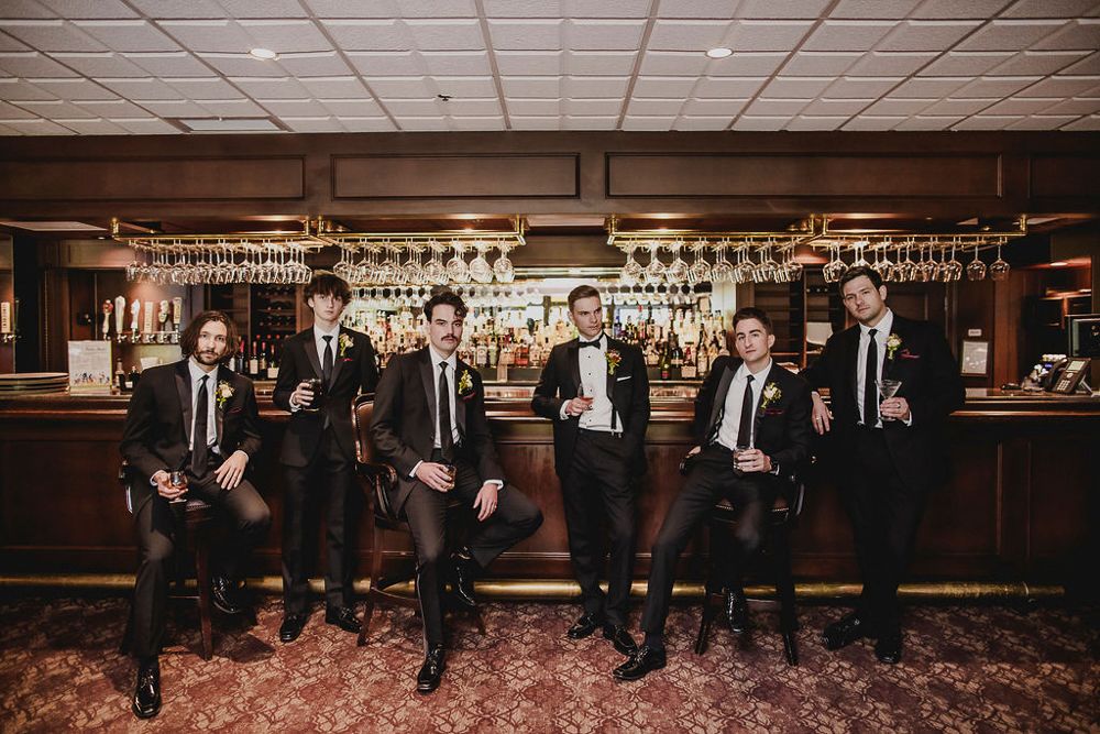 A series of wedding party photos showing groomsmen in dark suits posing in various formations at an indoor venue.