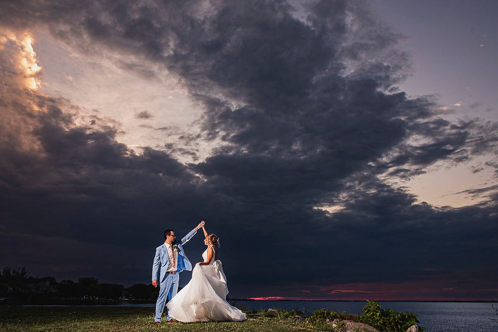 Dramatic sunset sky with dark storm clouds creates a moody backdrop for an outdoor wedding celebration.