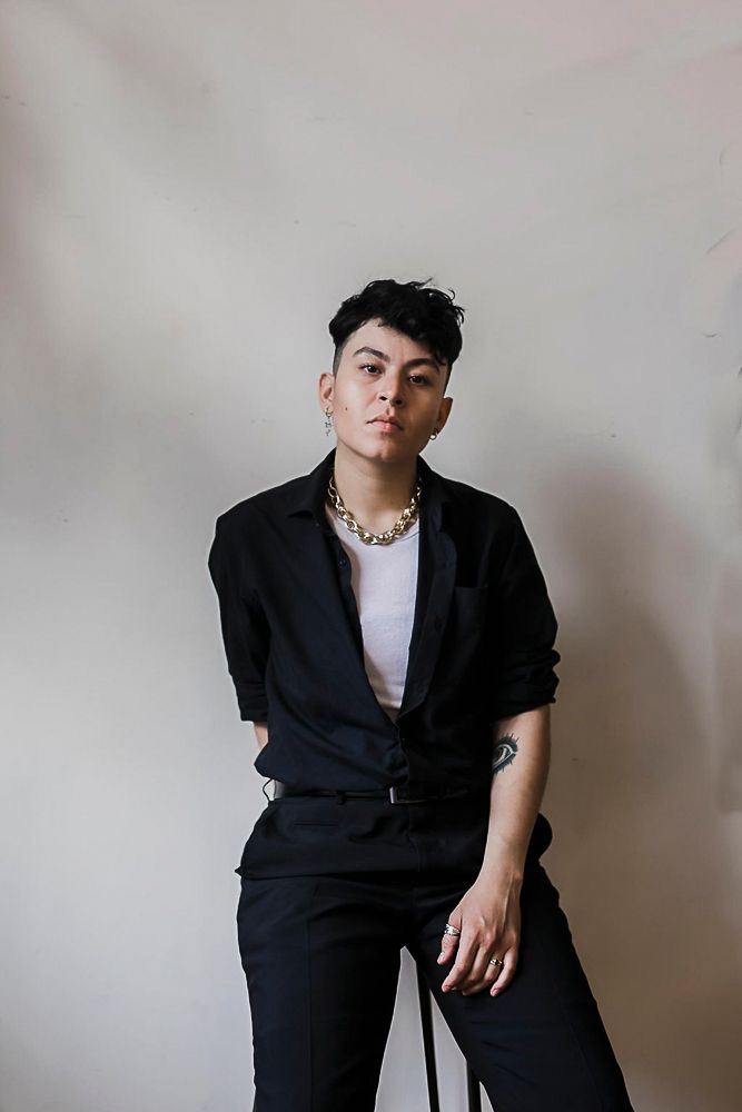 Androgynous fashion portrait with black blazer against neutral grey background.