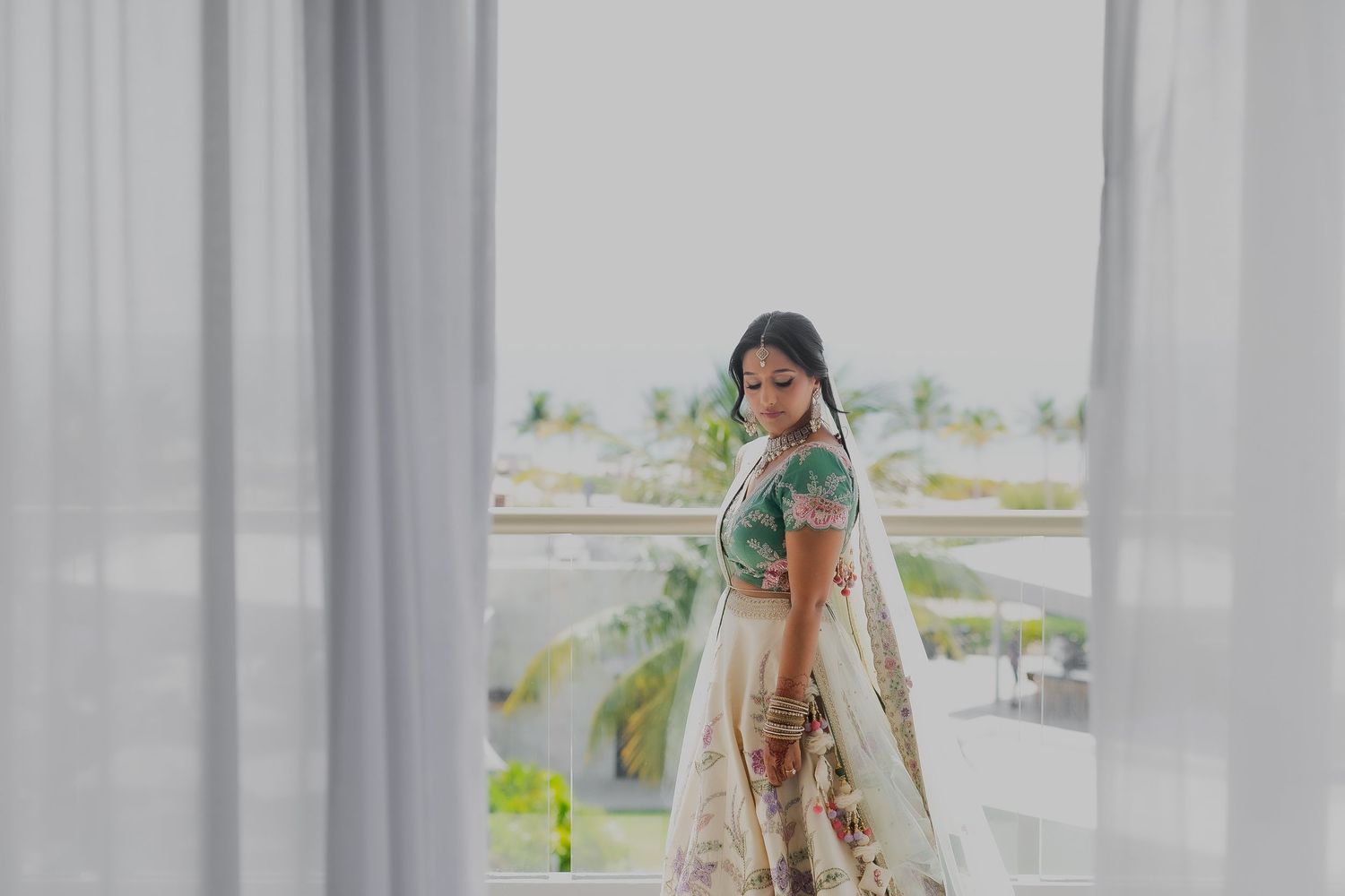 A traditional bride poses elegantly against white curtains with a scenic outdoor backdrop.