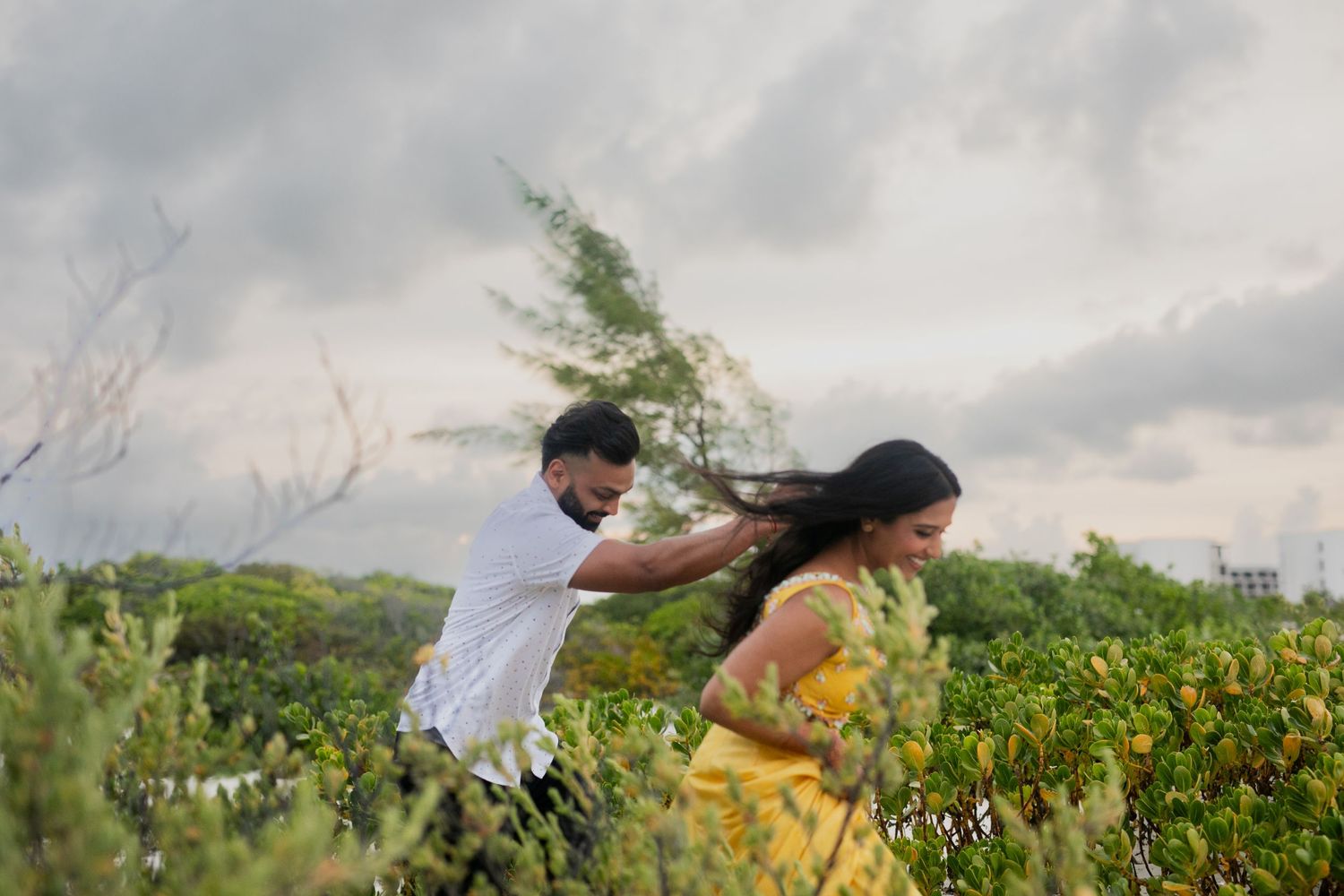 People walking through a lush green field with wildflowers under a cloudy sky.