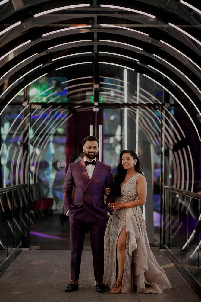 A couple in formal attire stands in a modern tunnel with illuminated arches and colorful lighting effects.