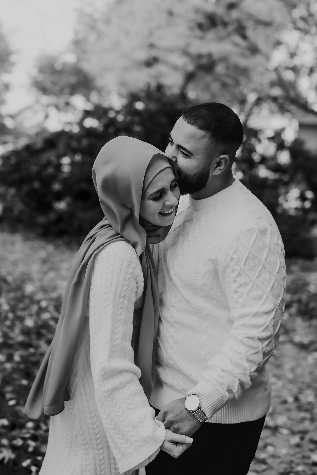 Black and white photo of a couple in white sweaters sharing an intimate moment outdoors during autumn.