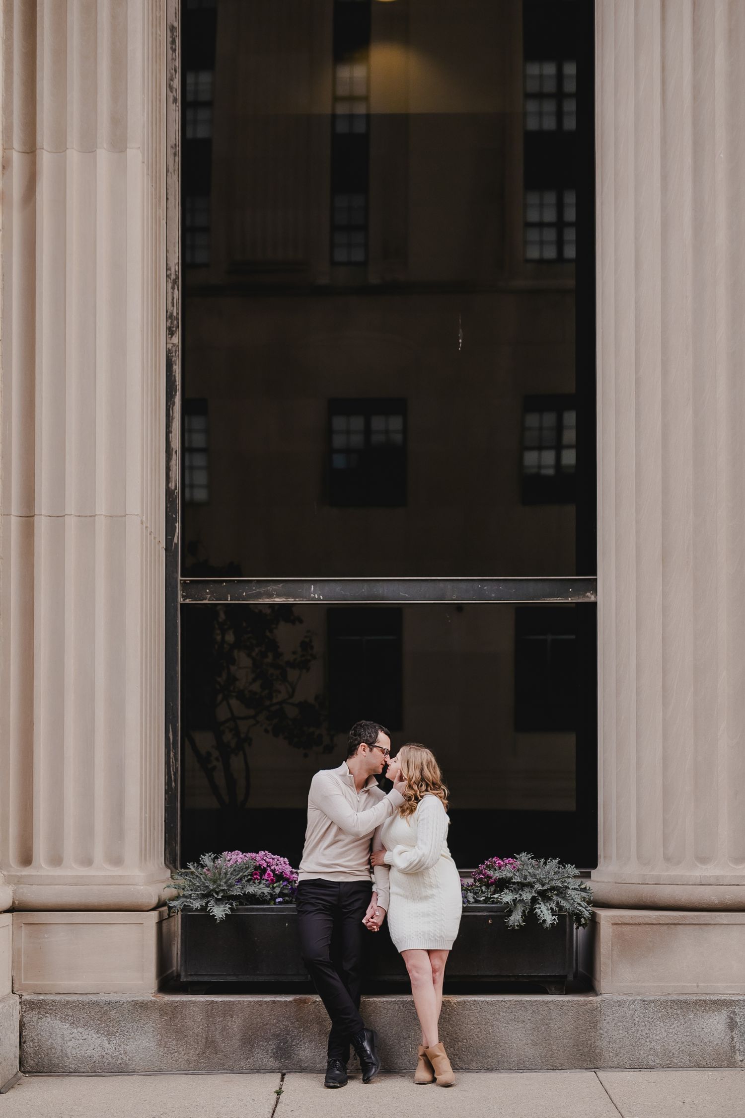 A couple shares a romantic moment between classical columns at an elegant building entrance.